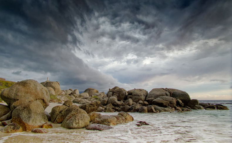 Coastal boulders and a sandy shore beneath dark clouds Coastal boulders and a sandy shore beneath dark clouds