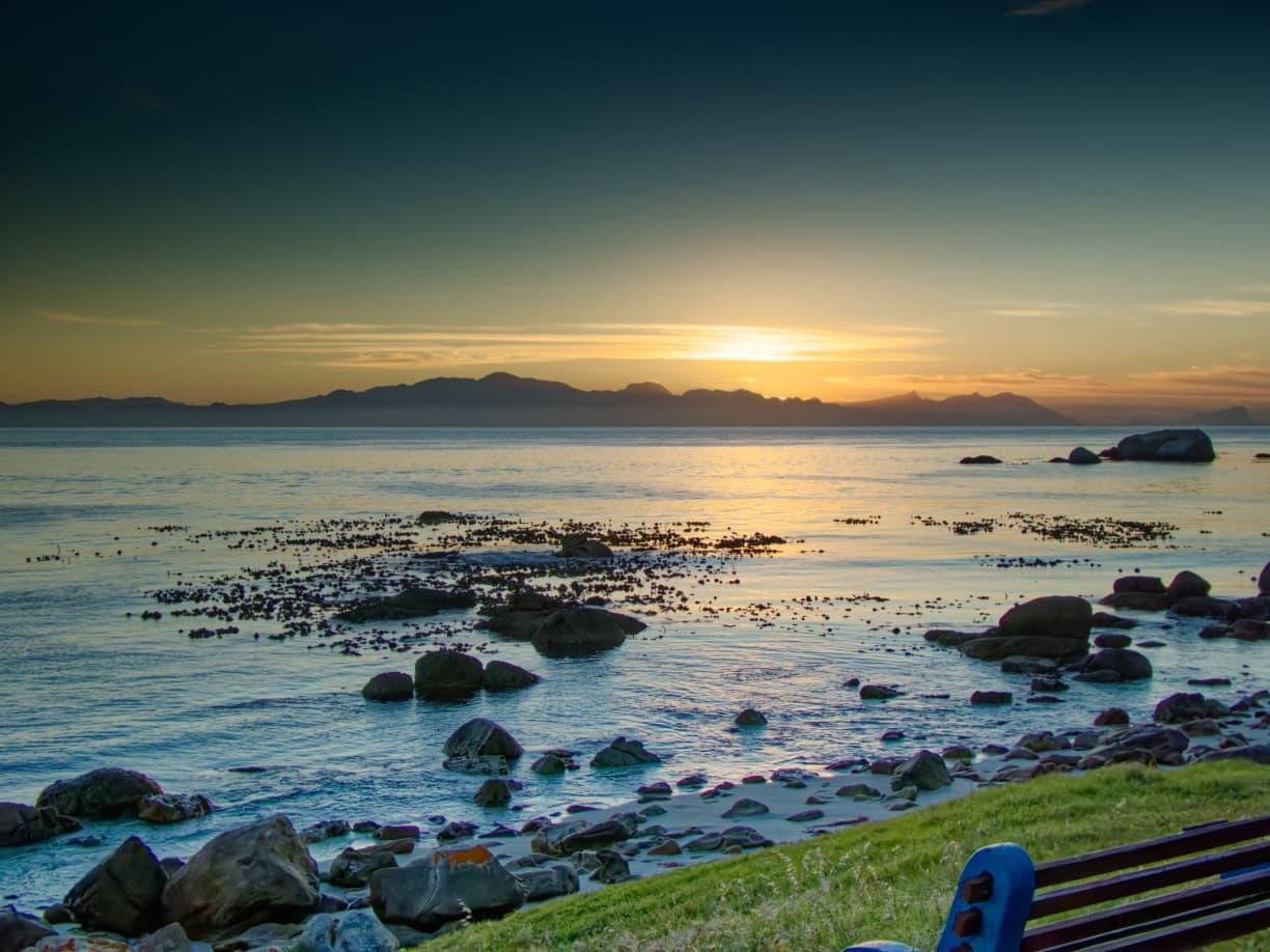 Golden sunrise over False Bay, with rocks and a bench along the shore