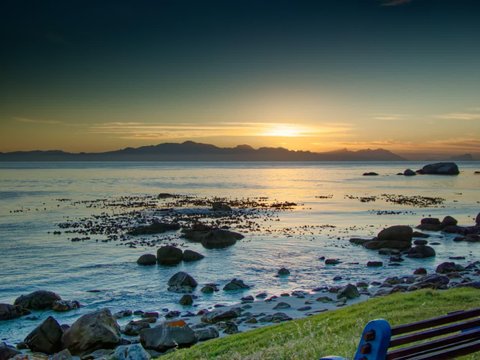 Golden sunrise over False Bay, with rocks and a bench along the shore