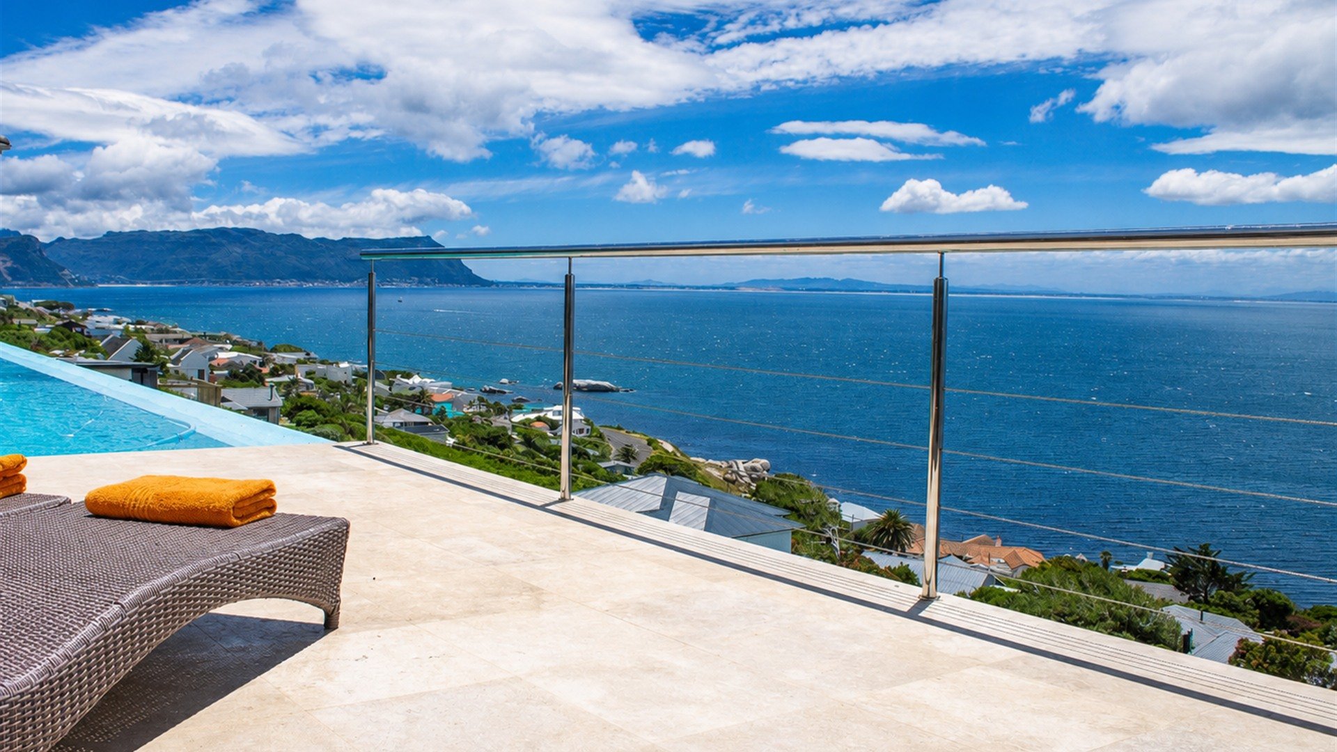 Sun lounger and orange towels on Aqua Terra's terrace overlooking False Bay, with the pool at the left