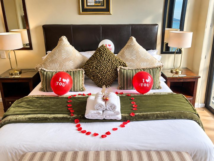 Bed decorated with rose petals, folded towels and red cushions
