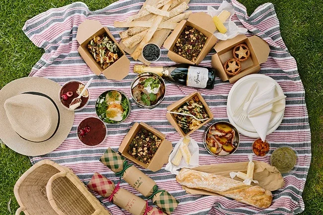 Picnic blanket with plates of food, bread and a bottle of wine