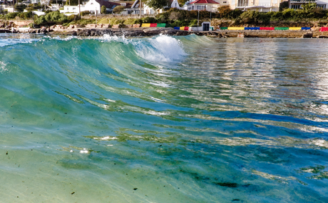 A small turquoise wave beside Fish Hoek waterfront houses and colourful benches