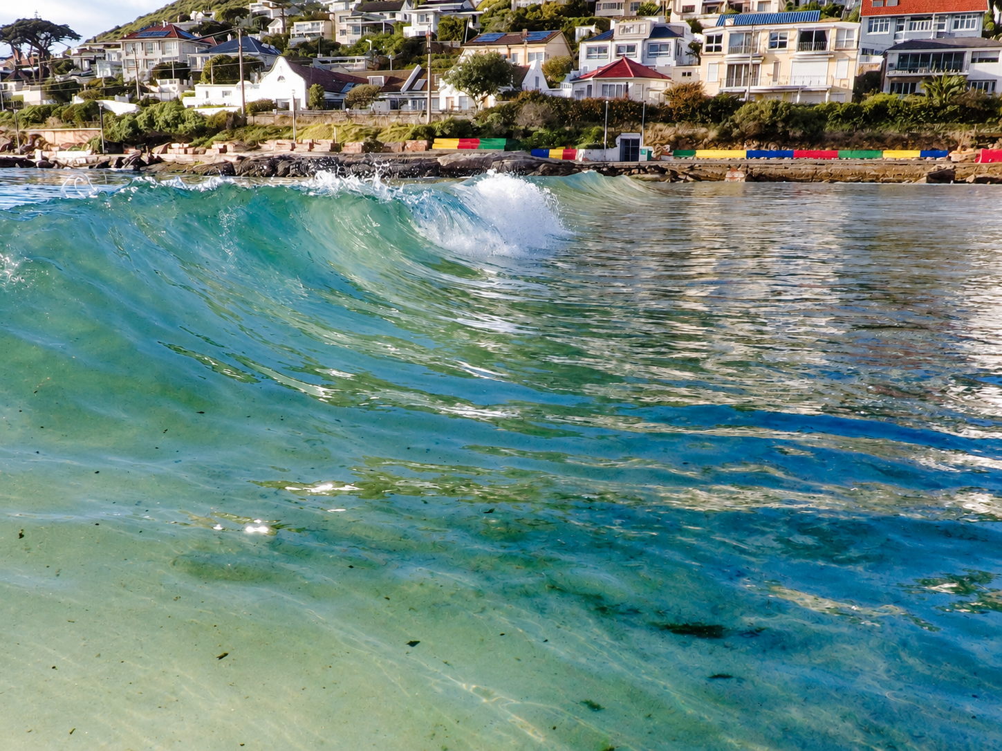 A small turquoise wave beside Fish Hoek waterfront houses and colourful benches