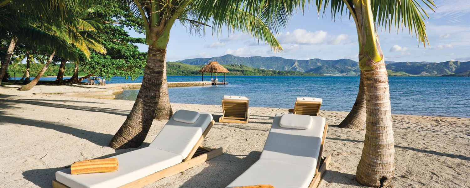 Moveable sun loungers shaded by palm trees on Dolphin Island beach