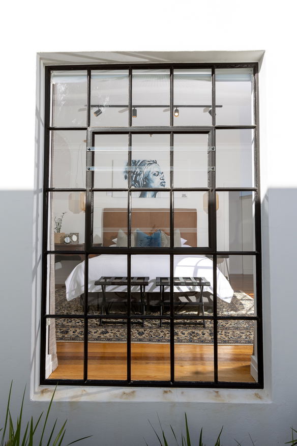 View from garden looking into guestroom at La Maison On Main in Paarl with king size bid and African artwork over the bed featuring Persian rug under the bed.