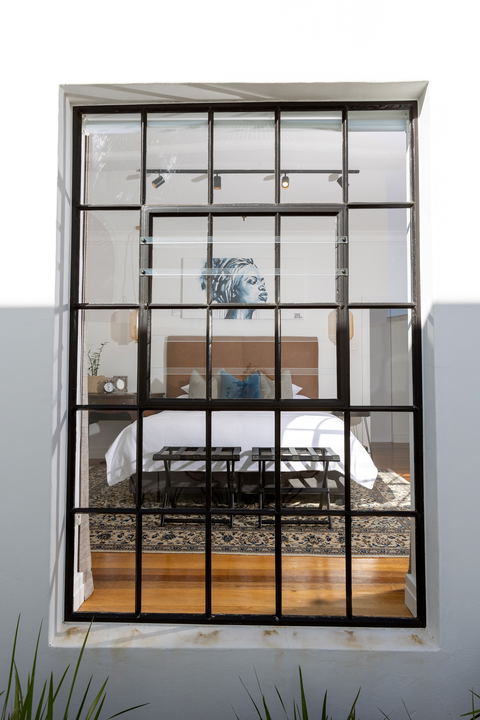 View from garden looking into guestroom at La Maison On Main in Paarl with king size bid and African artwork over the bed featuring Persian rug under the bed.