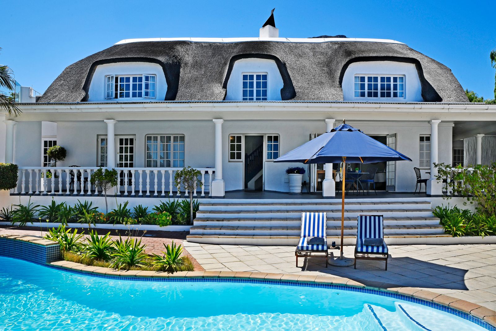 Thatched roof guesthouse at Guesthouse Mirabelle boutique accommodation in Franschhoek surrounded by garden and mountain scenery.