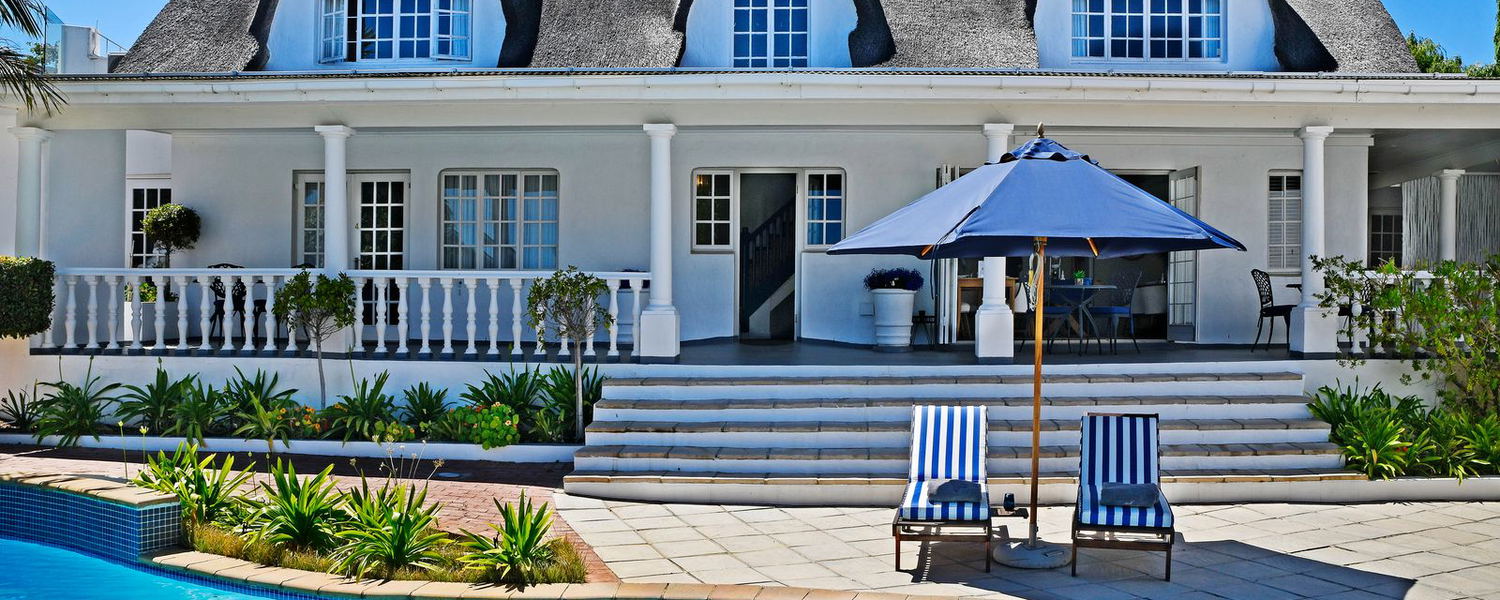 Thatched roof guesthouse at Guesthouse Mirabelle boutique accommodation in Franschhoek surrounded by garden and mountain scenery.
