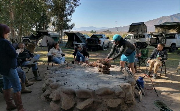 Campers sitting around a fire pit at Wolvenberg Boskamp at Wolvenberg & Stille Waters campsites, while a man is packing and starting a fire.