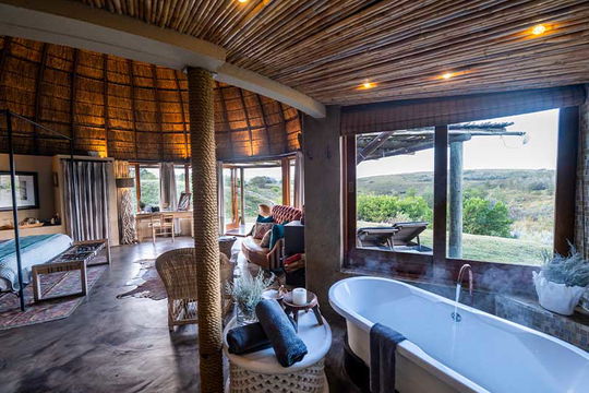 Escape to Gondwana Game Reserve, where breathtaking views from large windows and a soothing bathtub create the perfect retreat for couples to unwind and enjoy nature's beauty.