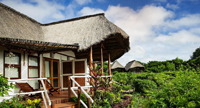 Luxury thatched-roof bungalow at Vilanculos Beach Lodge with a private wooden deck, lounge chairs, and tropical surroundings, offering a serene beachfront retreat.