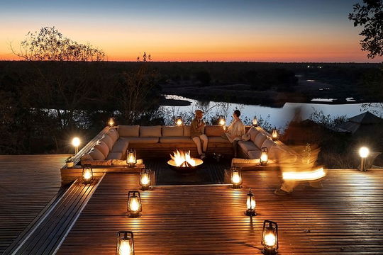 Simbavati Hilltop Lodge features a tranquil outdoor fountain illuminated by soft lighting, creating a serene nighttime atmosphere. Surrounded by trees and set against a beautiful sky at sunset or sunrise, this peaceful space invites relaxation and connection with nature.