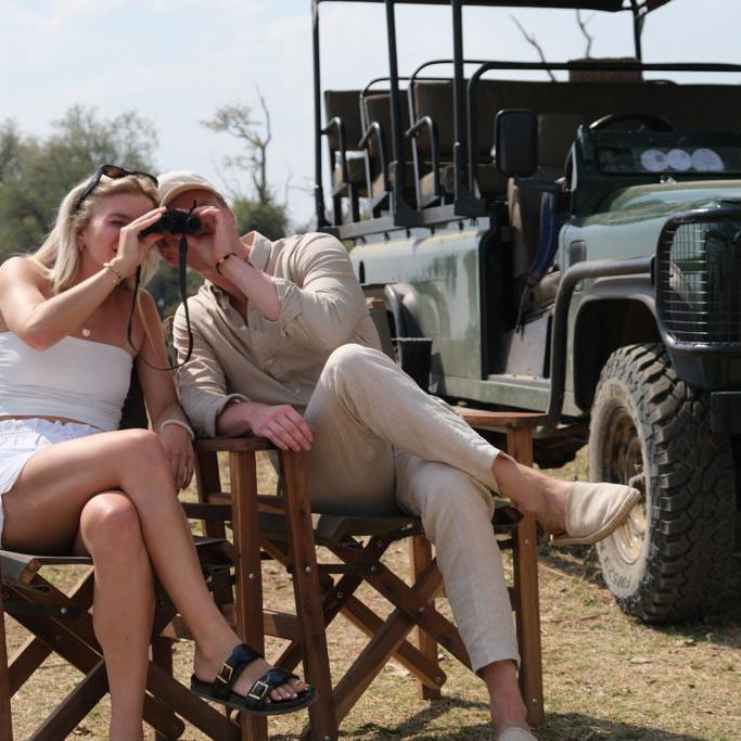 a couple watching through bino on a safari trip with lowani travel in Nsefu Area, South Luangwa National Park. Behind them is a green safari game viewer.