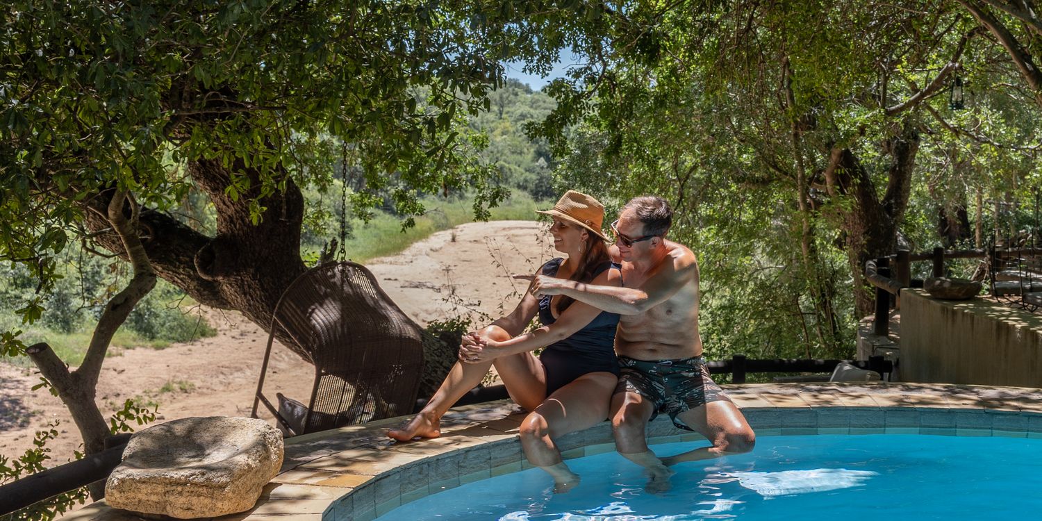 Honeymoon couple enjoying time at the Shimungwe Lodge pool with a view of the African bush