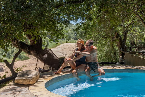 Honeymoon couple enjoying time at the Shimungwe Lodge pool with a view of the African bush Honeymoon couple enjoying time at the Shimungwe Lodge pool with a view of the African bush