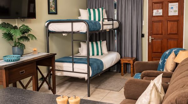 Coastal Apartment living area with bunk beds, comfortable seating, a wooden desk and wall-mounted TV at Amberlight Guesthouse in Krugersdorp.