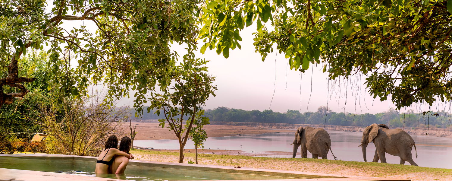 Boy and girl watching elephants cross the luangwa river