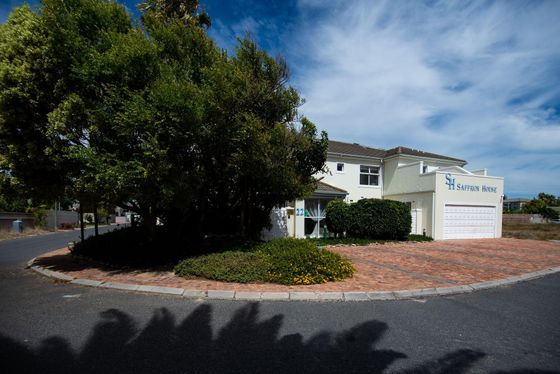 Two-storey cream guest house named Saffron House, with a white garage door and brick driveway under a large tree.