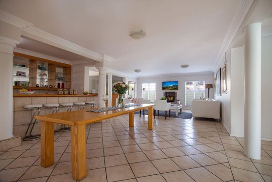 Open-plan lounge with a long wooden dining table, tiled floors, a bar with stools, and a fireplace with white sofas.