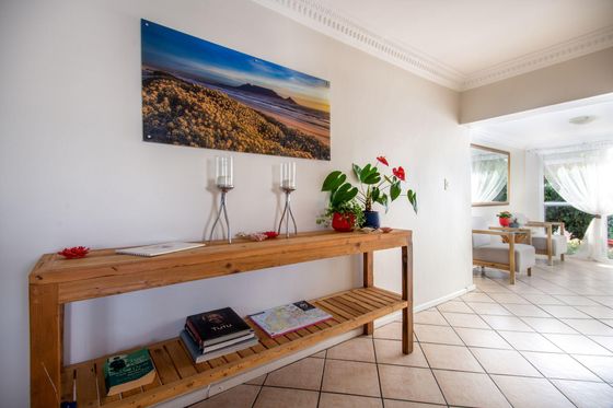 Wooden console table with books, candle holders and red flowering plants in a bright hallway leading to a sunlit lounge.