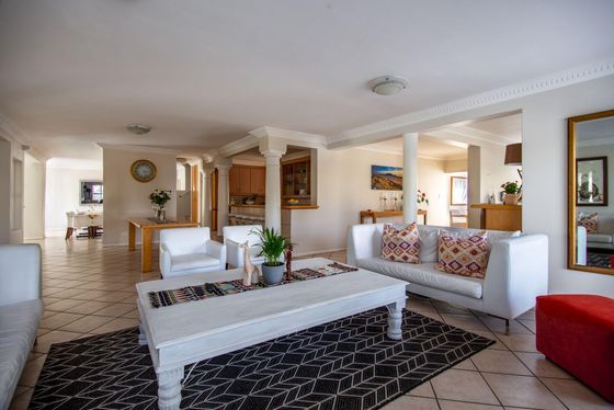 Spacious open-plan lounge with white sofas, a white coffee table, patterned cushions and a black geometric rug.