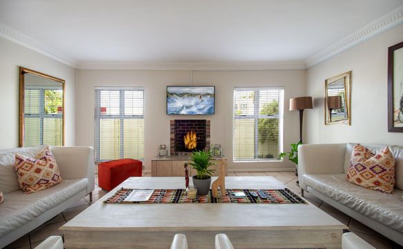 Living room with two white leather sofas, patterned cushions, a lit brick fireplace, and a wall-mounted TV.
