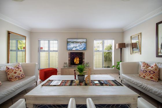 Living room with two white leather sofas, patterned cushions, a lit brick fireplace, and a wall-mounted TV.