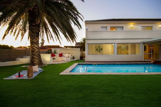 Two-story white house with a rectangular swimming pool and a palm tree on an artificial lawn at dusk.