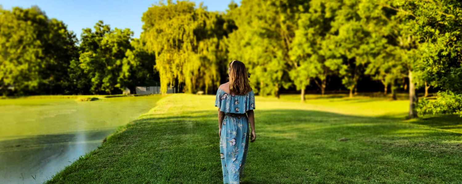 A lady walking on the dam wall next to a pecan orchard in the afternoon sun.