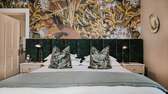 Double bed with dark green velvet headboard, two patterned cushions, and a botanical wall mural behind it.