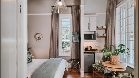 Studio apartment with a made bed, a kitchenette with a microwave, kettle and mini fridge, and a seating area by the window.