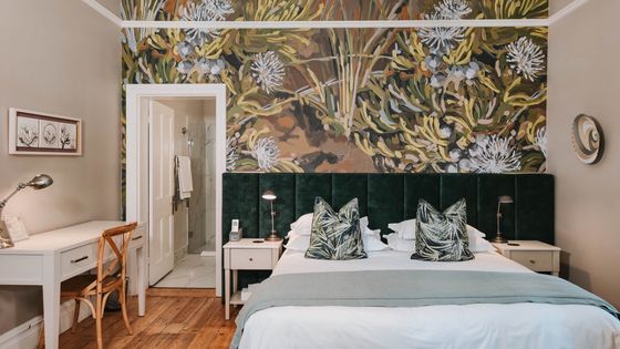 Bedroom with a king bed, dark green tufted headboard, leaf-print cushions, and a large botanical wall mural.