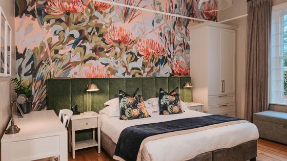 Bedroom with a large bed, green velvet headboard, and floral wall mural in pink and green tones.