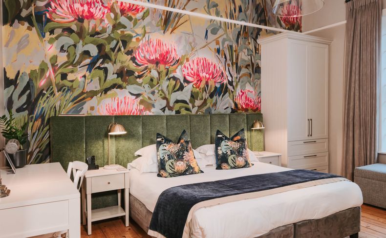 Guest bedroom with a king bed, green tufted headboard, and a floral wall mural of pink protea blooms.
