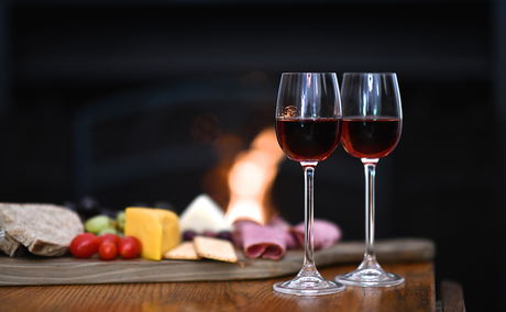 A warm and inviting scene at Bonne Esperance Guest House in Stellenbosch: two sherry glasses, a cheese board, and a roaring fireplace, perfect for winter evenings.