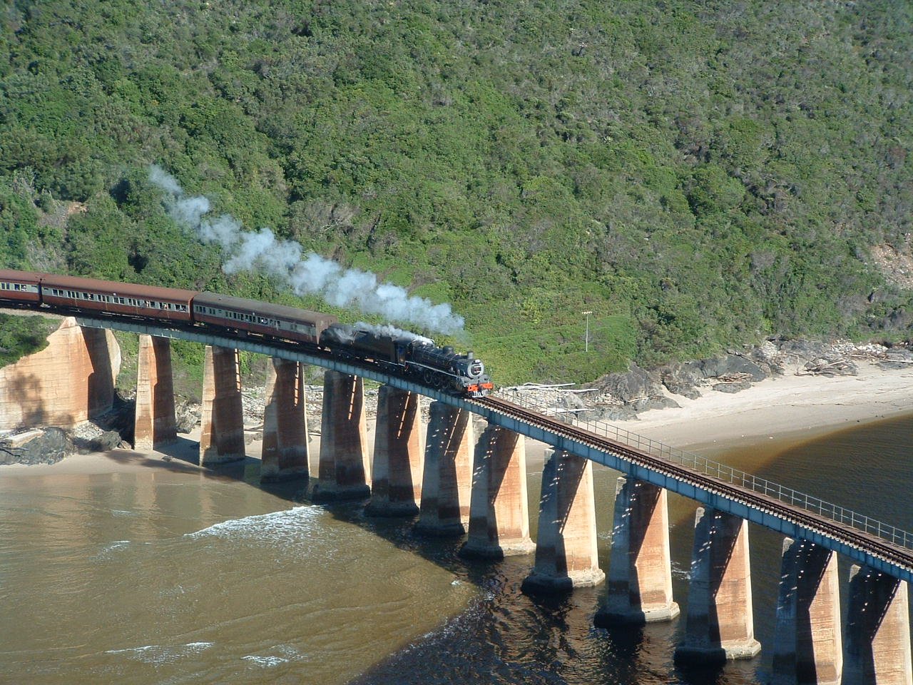Image: Tim Giddings - public domain. Outeniqua Choo Tjoe on the Kaaimans River Bridge. Photo taken some time before the line was shut down in 2006.