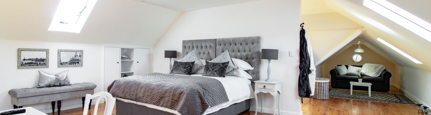 The king bed can be separated into two singles on request. A double sleeper couch is neatly tucked into one of the two alcoves. Natural light fills the room, while the wooden floors create a warm, welcoming atmosphere.