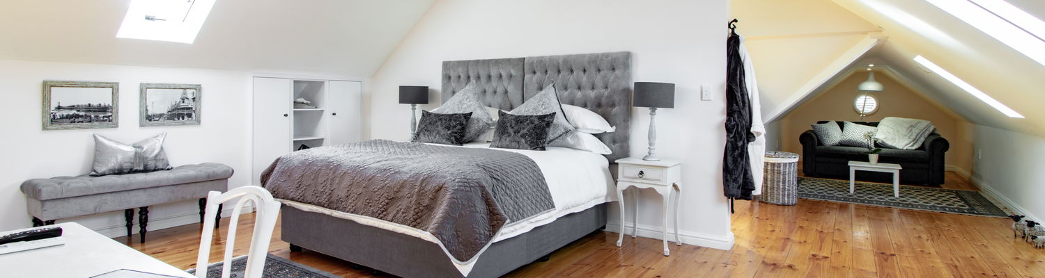 The king bed can be separated into two singles on request. A double sleeper couch is neatly tucked into one of the two alcoves. Natural light fills the room, while the wooden floors create a warm, welcoming atmosphere.