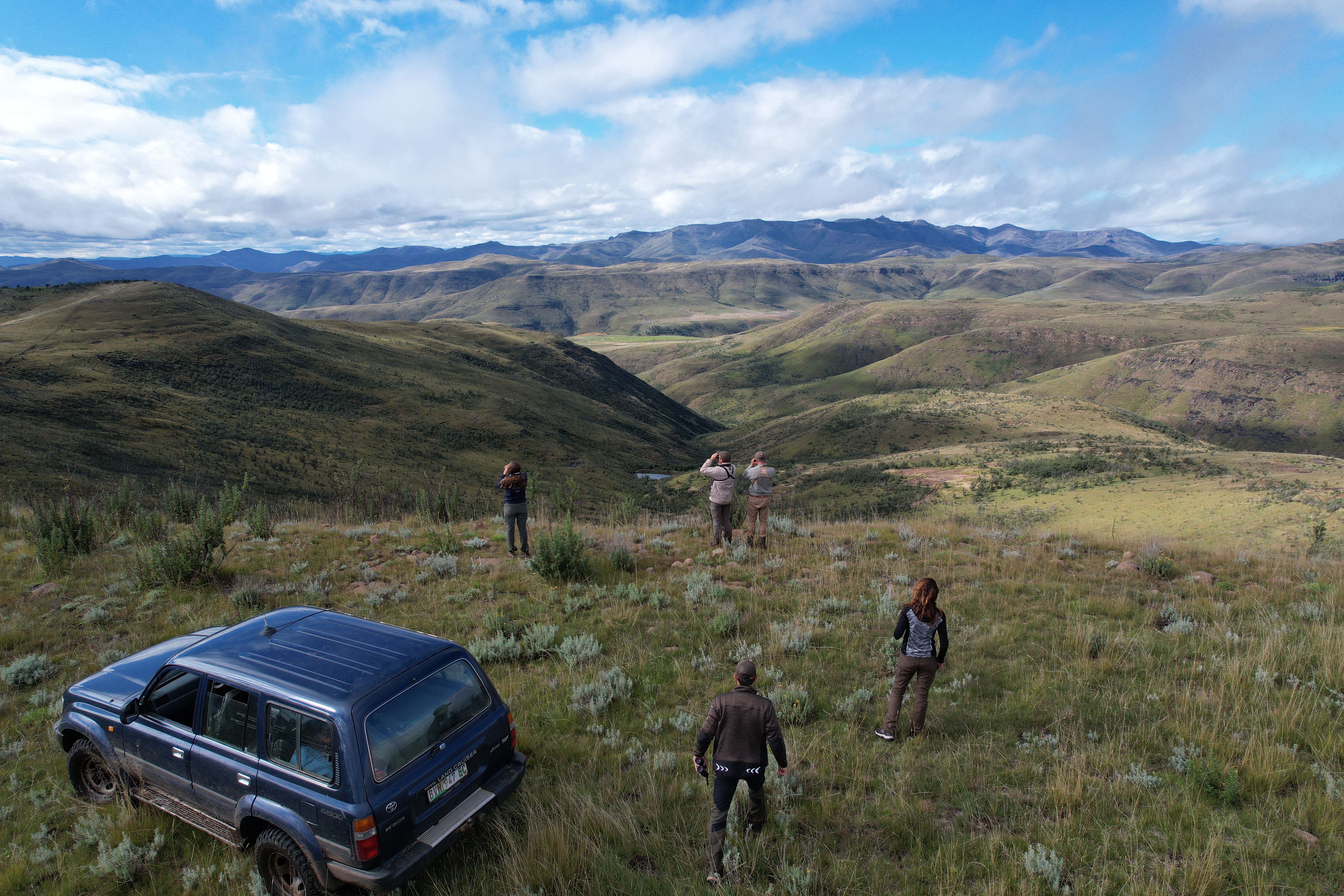 Aerial drone image showing hunters scanning the slopes for game in a pristine, high-altitude free-range hunting area. The rugged mountains, open ridgelines, and sweeping views highlight the unmatched beauty and scale of this wilderness.