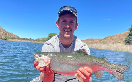 A fly fisherman casting in a clear mountain stream, surrounded by rugged scenery, while targeting wild Rainbow Trout in South Africa’s highlands.