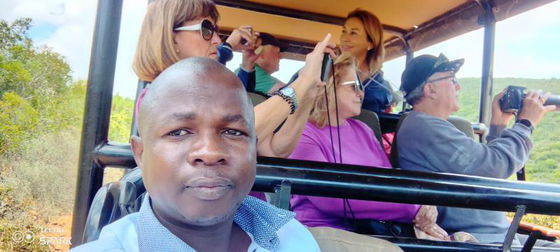 Smiling and approachable, this Into Tours accredited tourist guide is prepared to lead an unforgettable safari adventure in Addo and cultural experiences in Port Elizabeth. This picture is on an open vehicle safari with smiling guests taking a photograph of African wildlife and big 5 using their cameras 