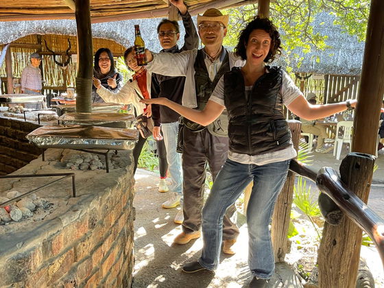 Janina, Into Tours director and tour guide, shares a fun moment with cruise ship guests on a perfectly organised tour. Smiles all around as they enjoy a cold local black label beer and traditional South African cuisine lunch before heading out on an open-vehicle safari at Schotia Private Game Reserve — the perfect mix of relaxation, local culture, and wildlife adventure.