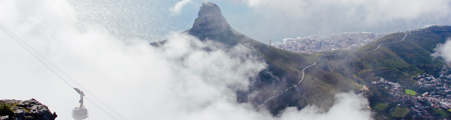 Cable car in Table Mountain with Signal Hill in the background and cover of clouds around the mountains with Cape Town city below