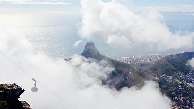 Cable car in Table Mountain with Signal Hill in the background and cover of clouds around the mountains with Cape Town city below 