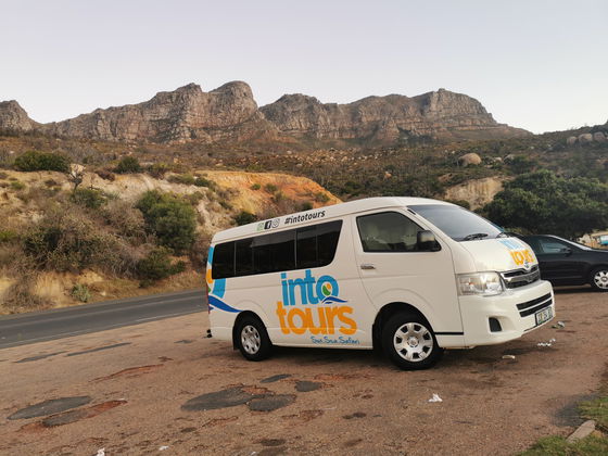 Visitors enjoying the scenic coastal drive in Cape Town in tour vehcile with magnificent 12 Apostles Mountain range behind at sunset .