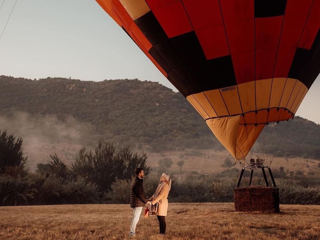 Couple standing on a field in front of a hot air balloon.