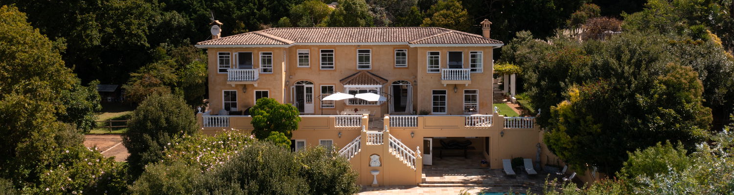 Devonport House in Constantia – elegant boutique guesthouse nestled against the lush slopes of Table Mountain, showcasing a classic Cape Dutch-inspired façade, serene terraces, and inviting pool surrounded by gardens.
