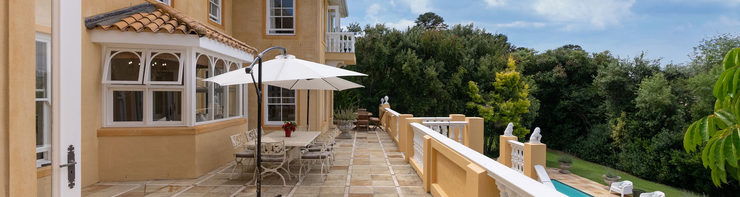Elegant outdoor patio at Devonport House in Constantia featuring a sunlit dining area with a large umbrella, perfect for alfresco breakfasts or relaxing afternoons. Surrounded by lush greenery, this serene space combines luxury, comfort, and nature for an unforgettable stay in Cape Town.