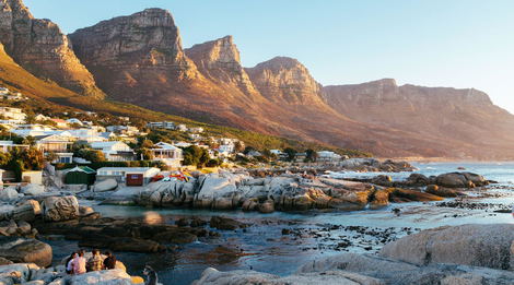 Tranquil coastal view of Bakoven Beach in Cape Town, with granite boulders, tidal pools, and the iconic backdrop of the Twelve Apostles mountains—just a scenic drive from Devonport House in Constantia. A serene, less-crowded spot ideal for sunset watchers and nature lovers.